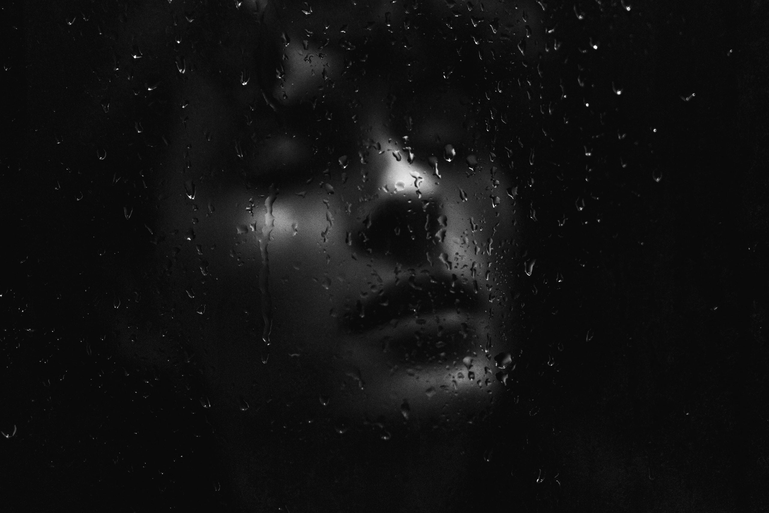 grayscale photography of man beside glass panel with water dew